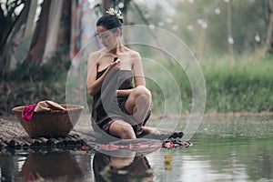 asian woman waering salong sitting on wooden bridge washing clothes in the river