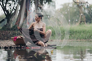 asian woman waering salong sitting on wooden bridge washing clothes in the river