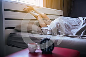 Asian woman wake up stretch oneself and yawn on her bedroom with blur black alarm clock