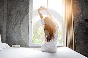 Asian woman waking up in her bed fully rested and open the curtains in the morning to get fresh air