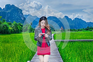 Asian woman walking on a wooden walkway with green rice fields in Vang Vieng, Laos