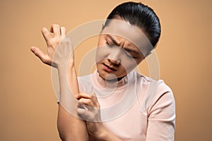 Asian woman was sick with irritate itching her skin standing isolated on beige background photo
