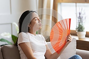 Asian woman waving fan cooling herself in hot weather indoors