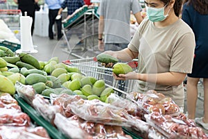 Asian woman wear a face mask,chooses necessary food,mango,fruit while shopping at supermarket,people panic buying, hoarding during photo