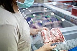 Asian woman wear face mask,choosing frozen pork food in freezer at supermarket,people panic buying and hoarding during the Covid-