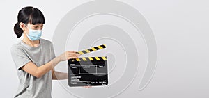 Asian woman wear face mask and hand`s holding black clapper board or movie slate or clapboard use in video production ,film,
