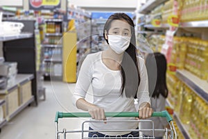 Asian woman wear face mask push shopping cart in suppermarket departmentstore. Girl choosing, looking grocery to buy  something.
