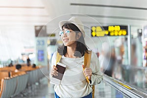 Asian woman wear glasses, hat with yellow backpack is holding flying ticket, passport at the hall of airport