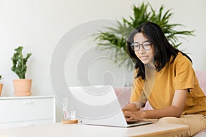 Asian woman wear glasses text work on laptop happy while sitting on sofa in living room at home