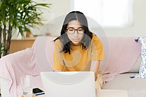 Asian woman wear glasses typing work on laptop. Asia student learn via internet with computer  while sitting on sofa in living