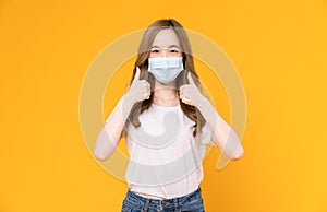Asian woman wear masks to protect disease and showing thumbs up or like on yellow background