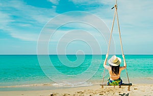Asian woman wear swimwear and hat swing the swings at sand beach  and looking beautiful tropical paradise sea and sky on sunny day