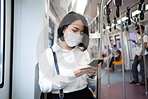 Asian woman wearing an anti-virus mask uses a smartphone to travel on a subway train as a COVID-19 outbreak occurs in the country