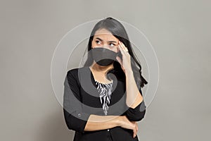 Asian woman wearing a black mask holding her head on the right