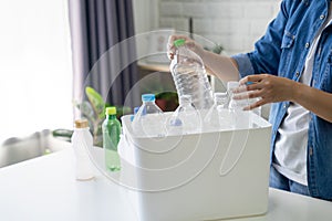 Asian woman wearing casual clothes sorting recycled plastic bottles into trash at home