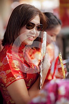 Asian woman wearing chinese tradition suit and holding bamboo fan with toothy smiling face in bangkok china town