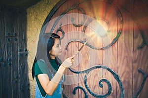 An Asian woman wearing in demin overalls standing and casting a spell at a wooden door
