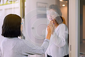 Asian woman wearing face shield with hands touching on window together,Stay at home during coronavirus and covid-19 epidemic or pa