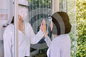 Asian woman wearing face shield with hands touching on window together,Stay at home during coronavirus and covid-19 epidemic or pa