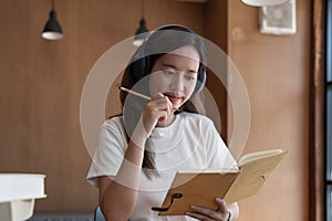 Asian woman wearing headphones watching webinar write notes on notepad. online education concept.