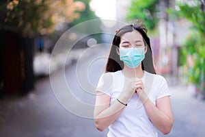 Asian woman wearing hygienic face mask for protection from air pollution or coronavirus praying by faith. Hands folded in prayer.