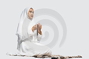 Asian woman wearing ihram clothes praying with prayer beads