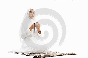 Asian woman wearing ihram clothes praying with prayer rug