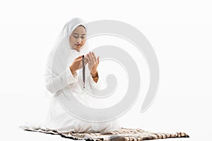 Asian woman wearing ihram clothes praying with prayer rug