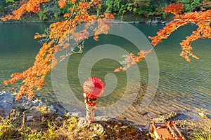 An Asian woman wearing Japanese traditional kimono with red umbrella standing with red maple leaves or fall foliage at Arashiyama