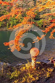 An Asian woman wearing Japanese traditional kimono with red umbrella standing with red maple leaves or fall foliage at Arashiyama