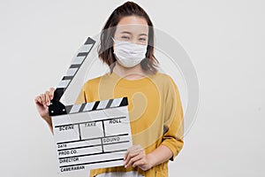 An Asian woman wearing a mask is holding a film clapper board.