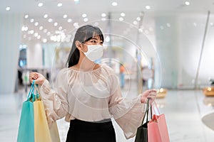 Asian woman wearing mask over her face while walking at shopping mall with shopping bag for healthcare and prevention from