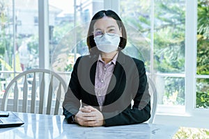 Asian woman wearing a mask sitting in the office wearing a black suit