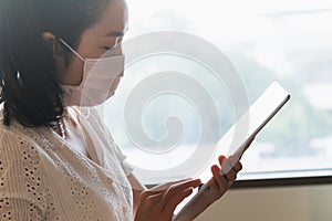 Asian woman wearing medical face mask, and using digital tablet