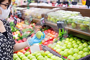 Asian woman wearing nitrile gloves and holding green apple fruit in supermarket or grocery, protect inflection.