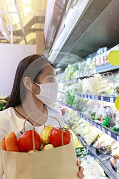 Asian woman wearing protective face mask hold paper shopping bag with fruits and vegetables in supermarket department store. Girl