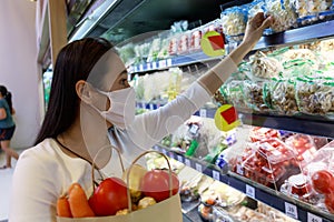 Asian woman wearing protective face mask hold paper shopping bag with fruits and vegetables in supermarket department store. Girl