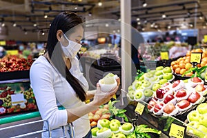 Asian woman wearing protective face mask hold paper shopping bag with fruits and vegetables in supermarket department store. Girl