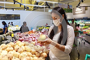 Asian woman wearing protective face mask hold paper shopping bag with fruits and vegetables in supermarket department store. Girl