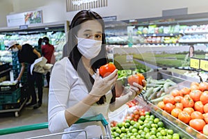 Asian woman wearing protective face mask hold paper shopping bag with fruits and vegetables in supermarket department store. Girl