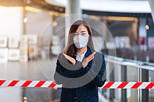 An asian woman wearing protective face mask, making crossed arms sign in front of red and white warning tape area