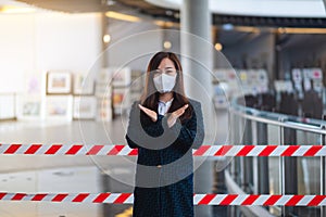 An asian woman wearing protective face mask, making crossed arms sign in front of red and white warning tape area