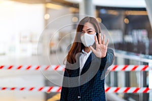 An asian woman wearing protective face mask, making stop hand sign in front of red and white warning tape area