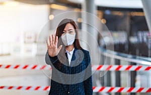 An asian woman wearing protective face mask, making stop hand sign in front of red and white warning tape area