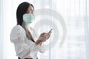 Asian woman wearing protective face mask, and using mobile smartphone