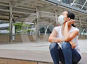 Asian woman wearing protective mask to protect virus, pollution and the flu sitting at public area