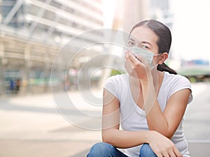 Asian woman wearing protective mask to protect virus, pollution and the flu sitting at public area