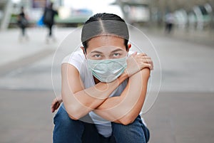 Asian woman wearing protective mask to protect virus, pollution and the flu sitting at public area