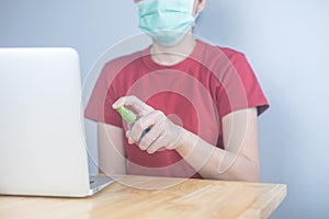 Asian woman wearing protective mask using spray alcohol sanitizer cleaning a computer, to prevent the virus and bacterias, woman