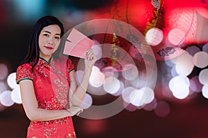 Asian woman wearing red traditional dress holding red pocket with the chinese new year festival background with lanterns
